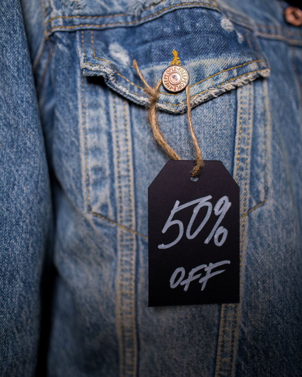 Veste en jean soldée : une étiquette noire « 50 % off » pend à la poche de poitrine, attachée par une ficelle.