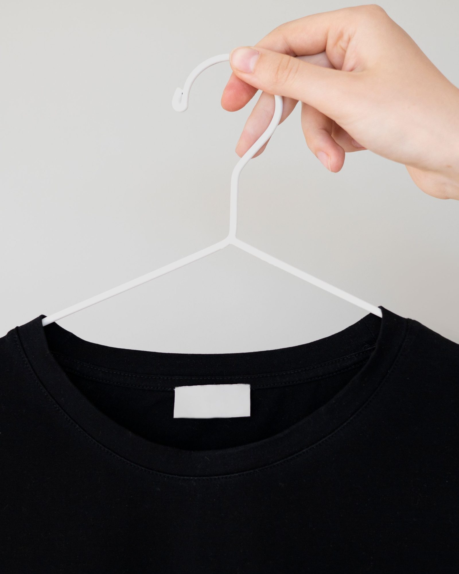 Une main retourne l’étiquette d’un t-shirt vert d’eau suspendu à un portant.